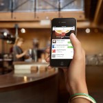Photo of a woman at a coffee shop who is about to make a purchase using the Pay with Square app on an iPhone